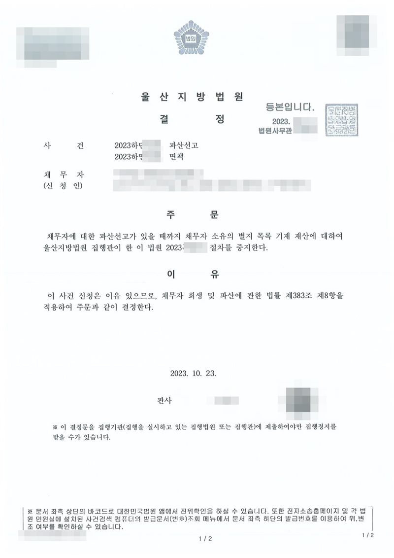 울산지방법원 결정. 사건명 파산선고와 면책. 주문은 채무자에 대한 파산선고가 있을 때까지 채무자 소유의 별지 목록 기재 재산에 대하여 울산지방법원 집행관이 한 이 법원 절차를 중지한다는 내용. 이유는 채무자 회생 및 파산에 관한 법률 제383조 제8항. 아래에 이 결정문을 집행기관에 제출하여야만 집행정지를 받을 수 있다는 안내가 있다. 집행 사건번호도 가렸다. 채무자 이름·주민등록번호·주소·사건번호 숫자·판사와 법원사무관 이름·판사 도장·파산관재인 이름·QR코드·발급번호·위변조 방지 바코드는 가렸다.